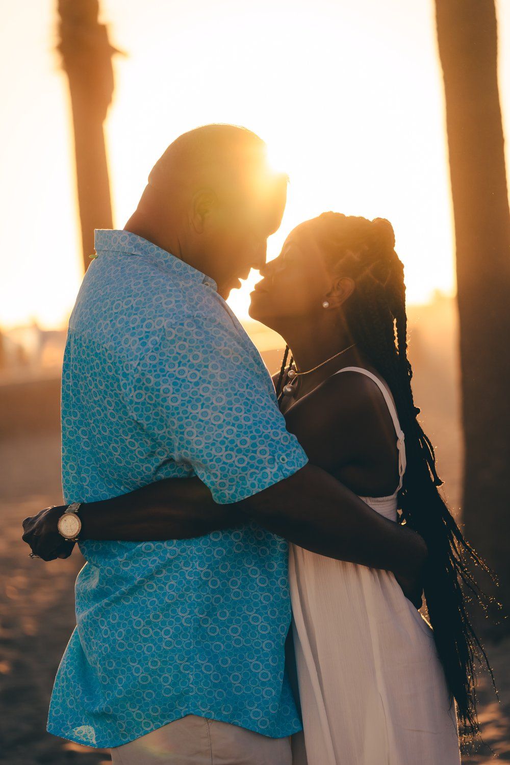 Couple embracing in warm sunset light at huntington beach with backlit silhouettes.