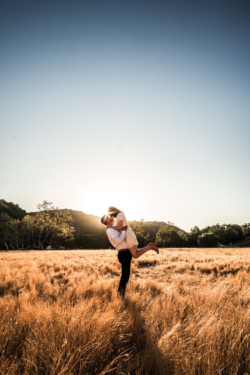 Couple embracing in golden field at sunset with mountains in background at Ronald W. Caspers Wilderness Park.