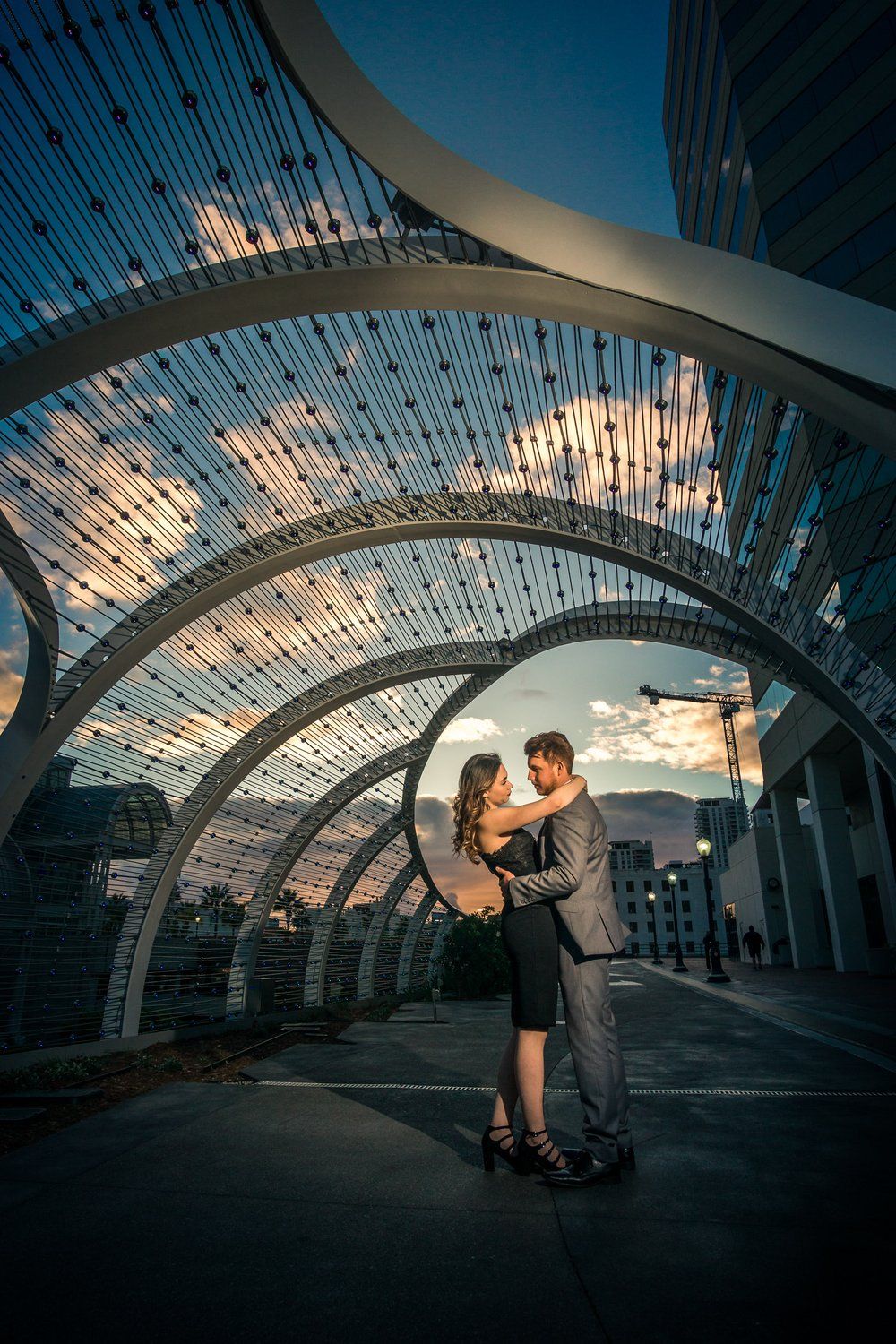 Couple embracing under illuminated architectural arches at sunset in an urban setting.