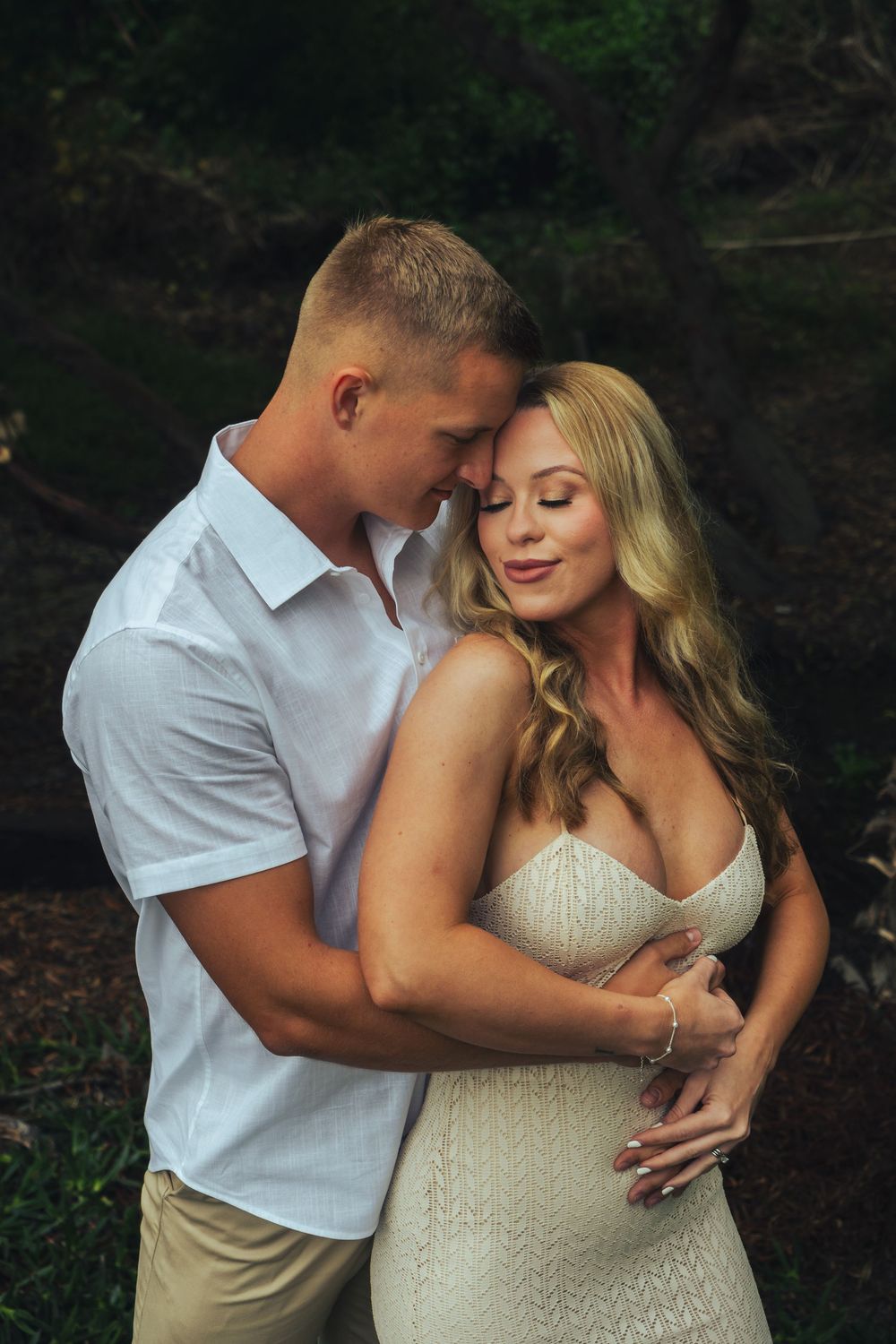A romantic outdoor portrait shows a couple embracing intimately, with her wearing a white dress and him in a white shirt at laguna beach.