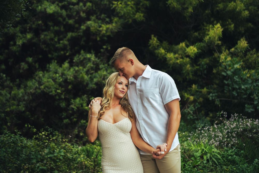 A romantic couple in casual wedding attire embrace while sharing a tender moment in a lush garden at table rock , laguna beach
