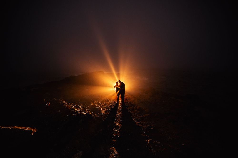 A silhouette stands on a mountain summit backlit by a dramatic glowing sunset creating an ethereal panorama at table rock, laguna beach