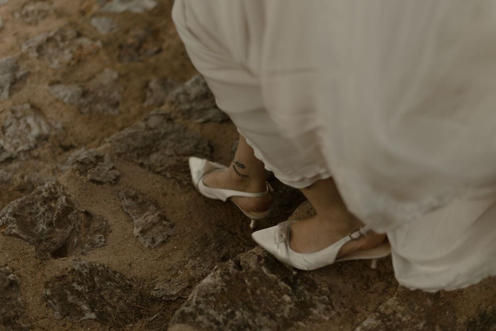 Close-up of white lace wedding dress hem trailing over brown soil ground with decorative beading details.