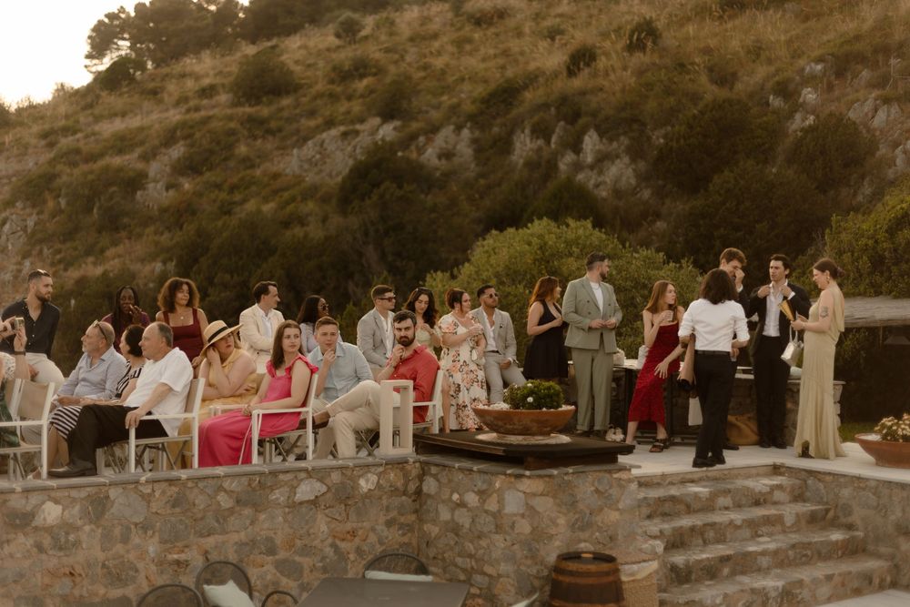 Wedding guests gather on rustic stone steps during an outdoor celebration at sunset in a mountainous location.