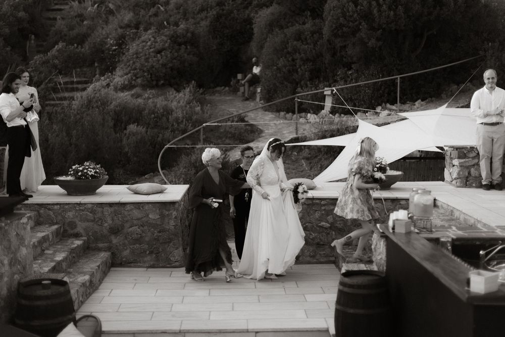 Outdoor wedding reception with multiple round tables set up on a stone patio surrounded by lush greenery at sunset.