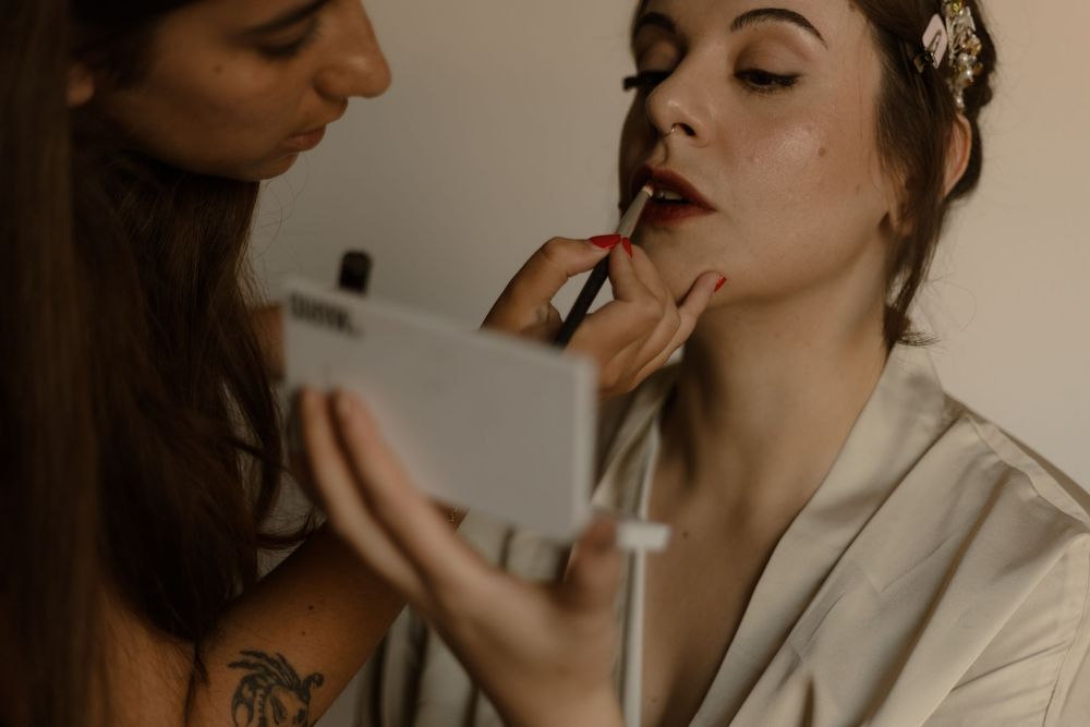 A makeup artist applies lipstick to a woman wearing a light robe during wedding preparation.