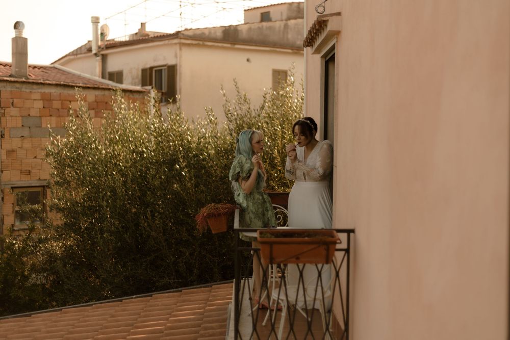 Two people share a romantic moment on an outdoor terrace overlooking a scenic Mediterranean landscape at sunset.