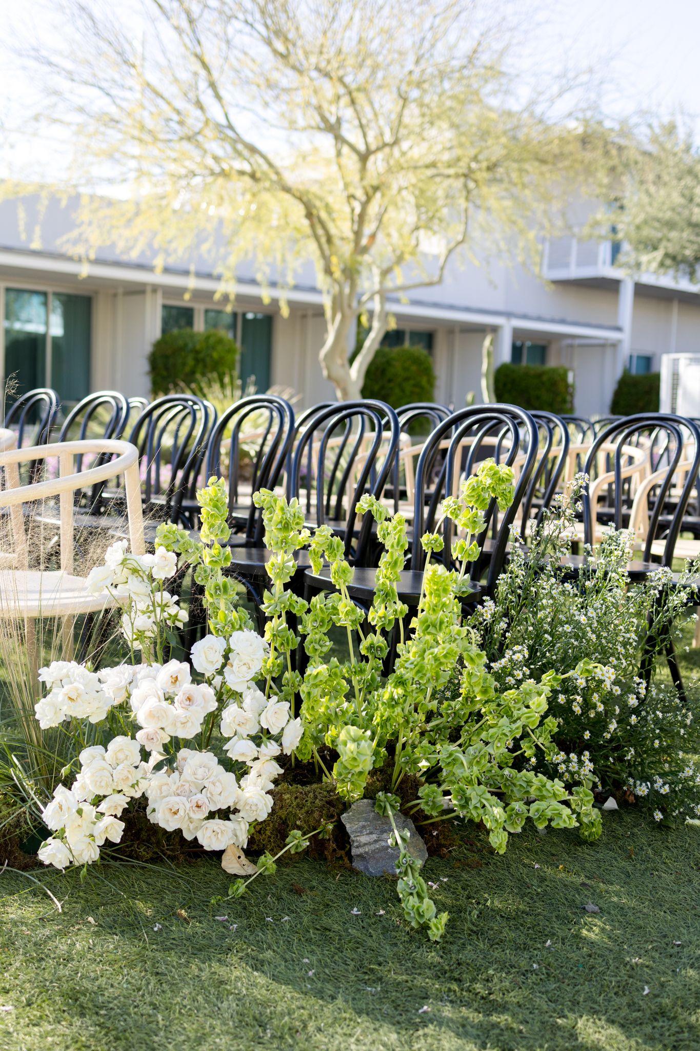Elegant outdoor wedding setup with black bistro chairs and lush white and green floral arrangements on the lawn.