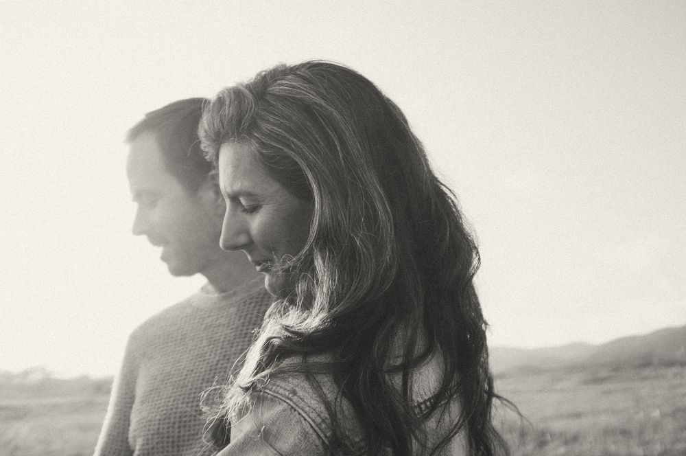 Black and white artistic portrait of a couple silhouetted against a mountain landscape in romantic pose.
