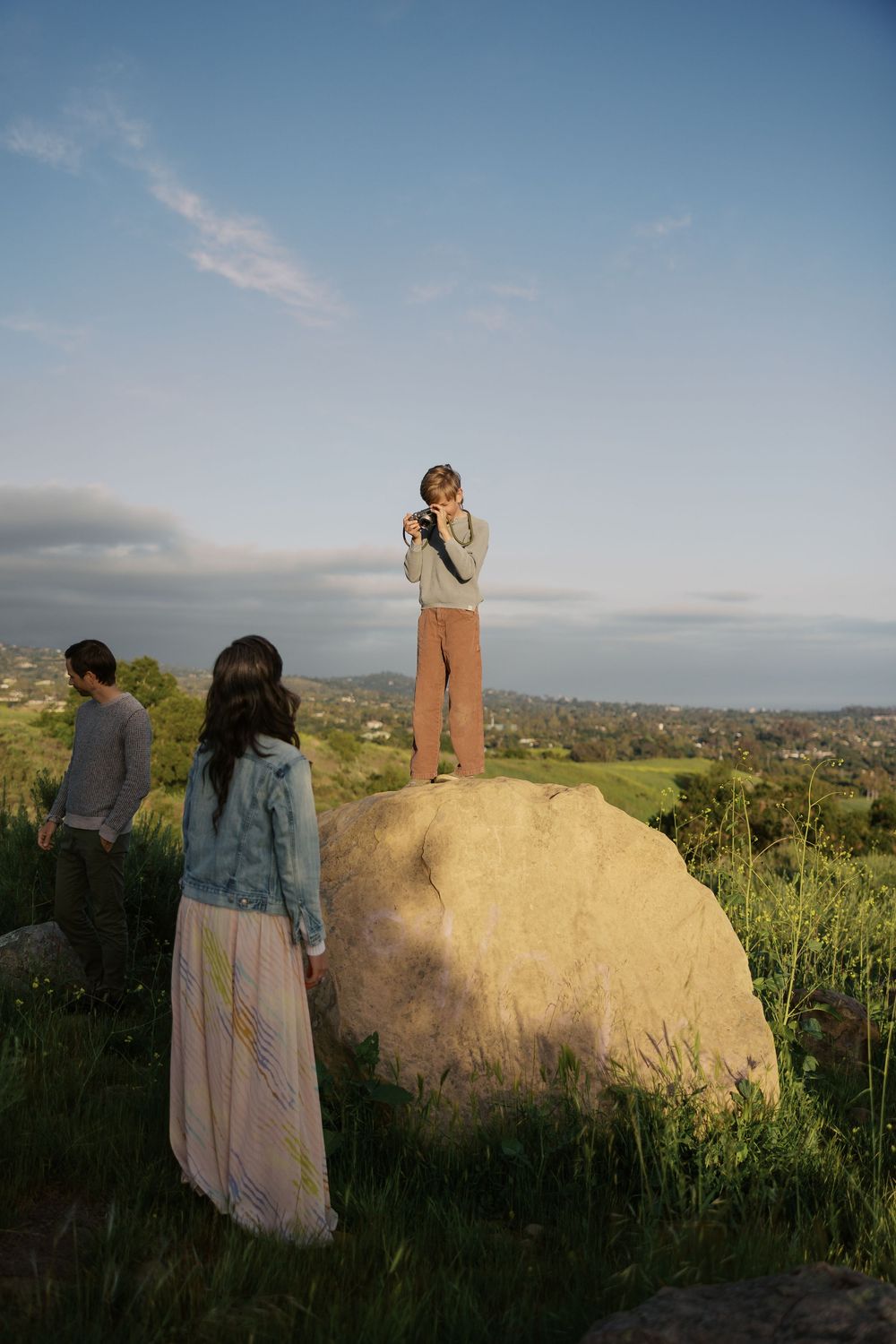 A couple stands at sunset on a scenic overlook surrounded by desert landscape and distant mountains.
