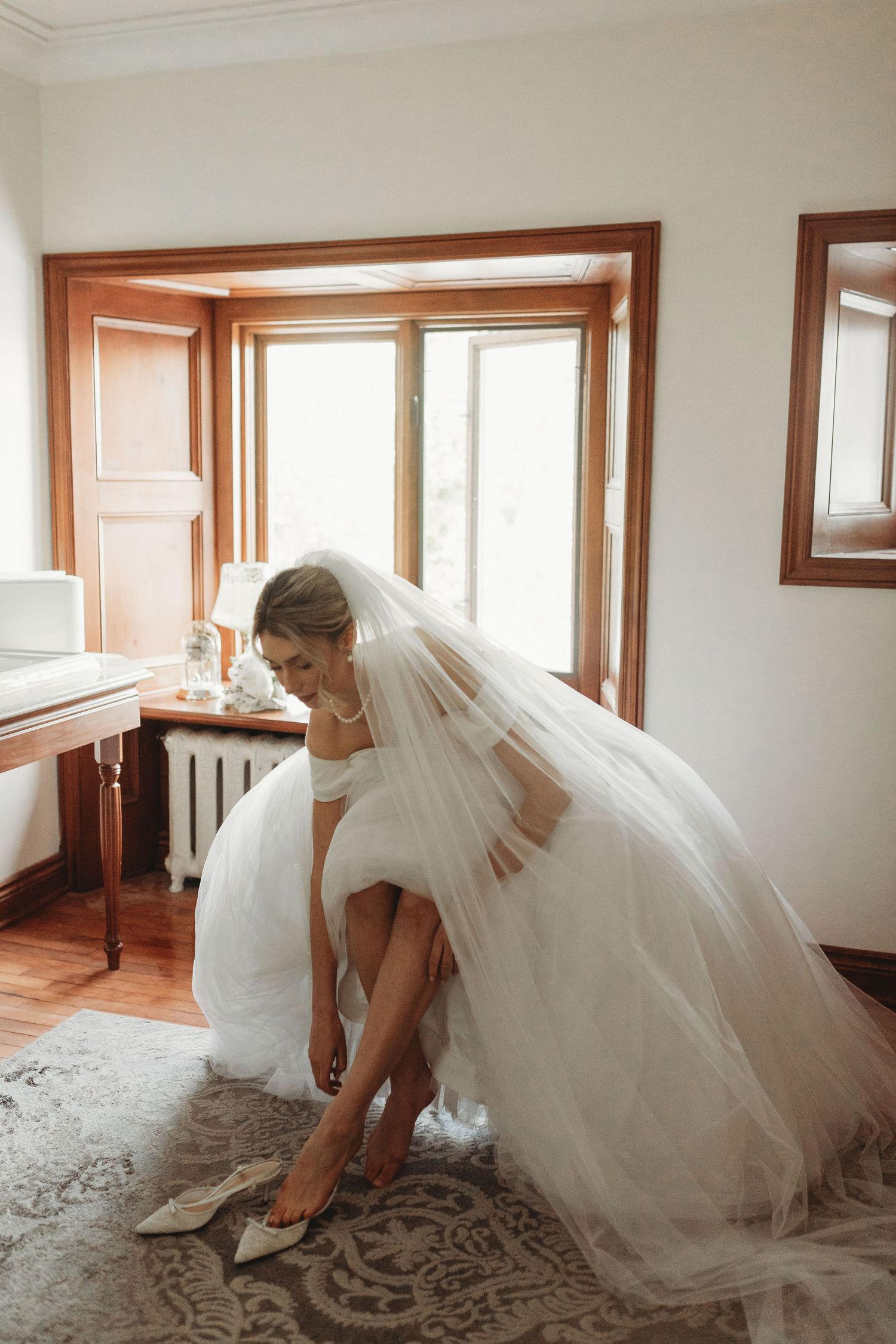 A candid moment of bridesmaids in mint green dresses admiring the bride's flowing white veil during wedding preparations.