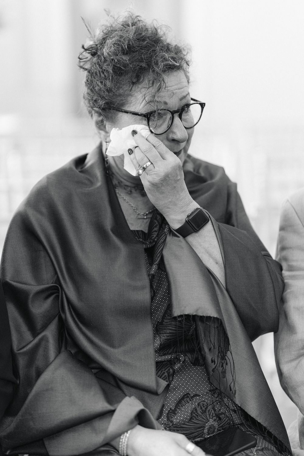 A person in glasses and dark clothing shows an emotional reaction during what appears to be a special event.