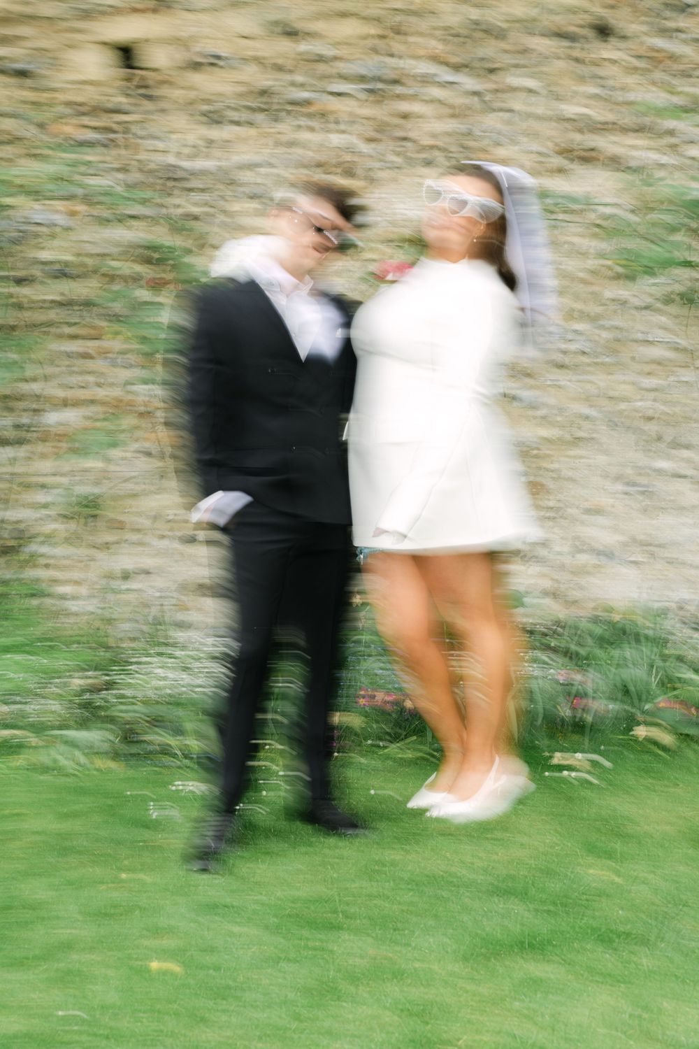 Motion blur image sequence shows couple dancing on grass with person in dark suit spinning partner in white dress.