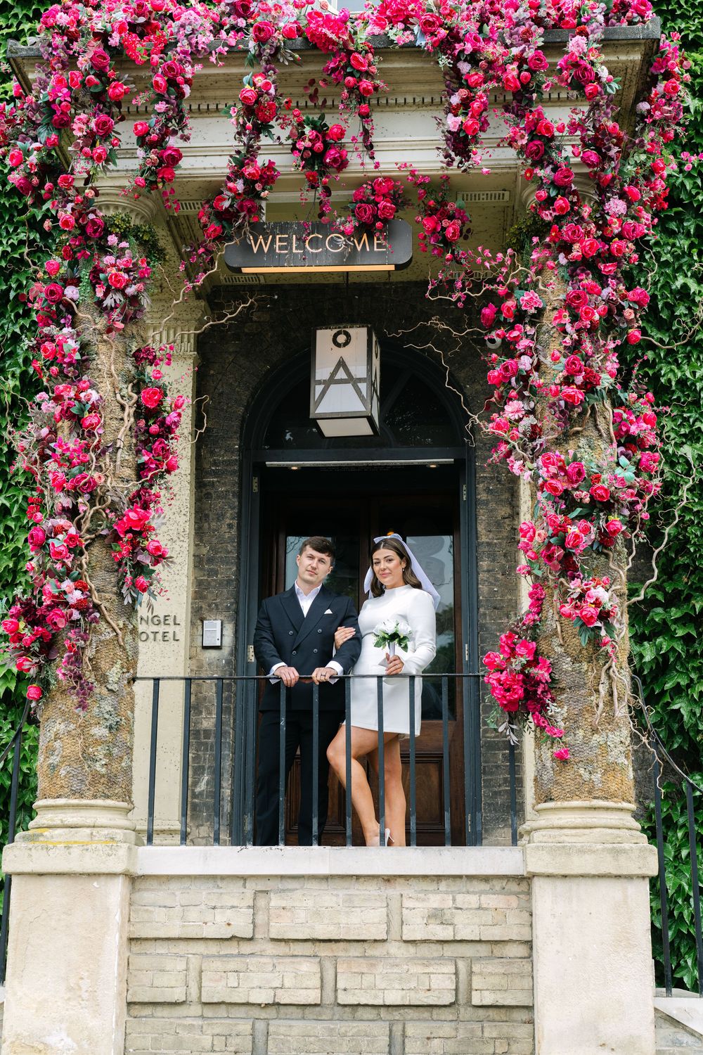 Beautiful stone archway entrance adorned with vibrant pink climbing roses and greenery creates a romantic garden setting.