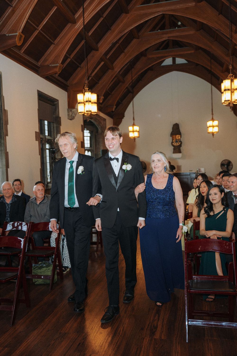 Wedding guests process into church sanctuary with wooden beam ceiling and hanging lights.