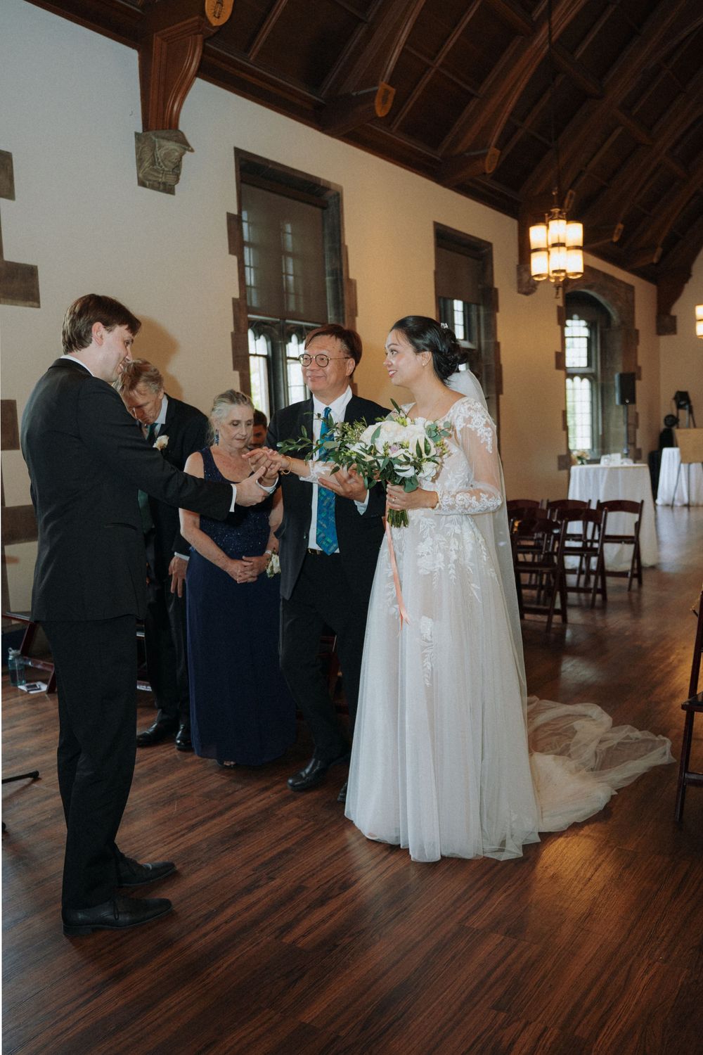 Wedding party members gathered in spacious hall with hardwood floors and hanging lanterns.