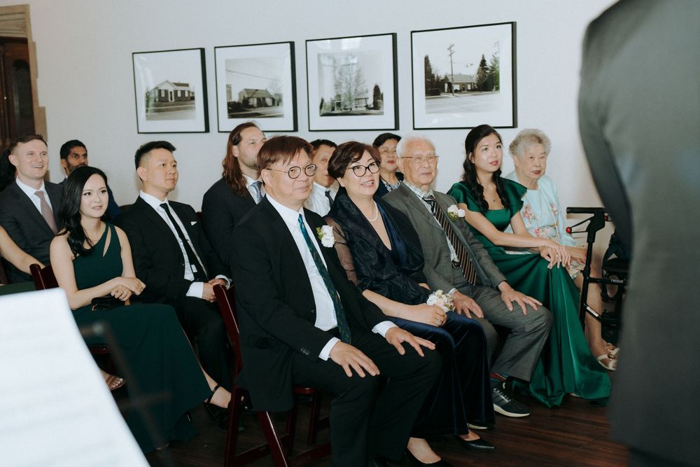 Wedding guests observing ceremony in front of wall decorated with framed artwork.