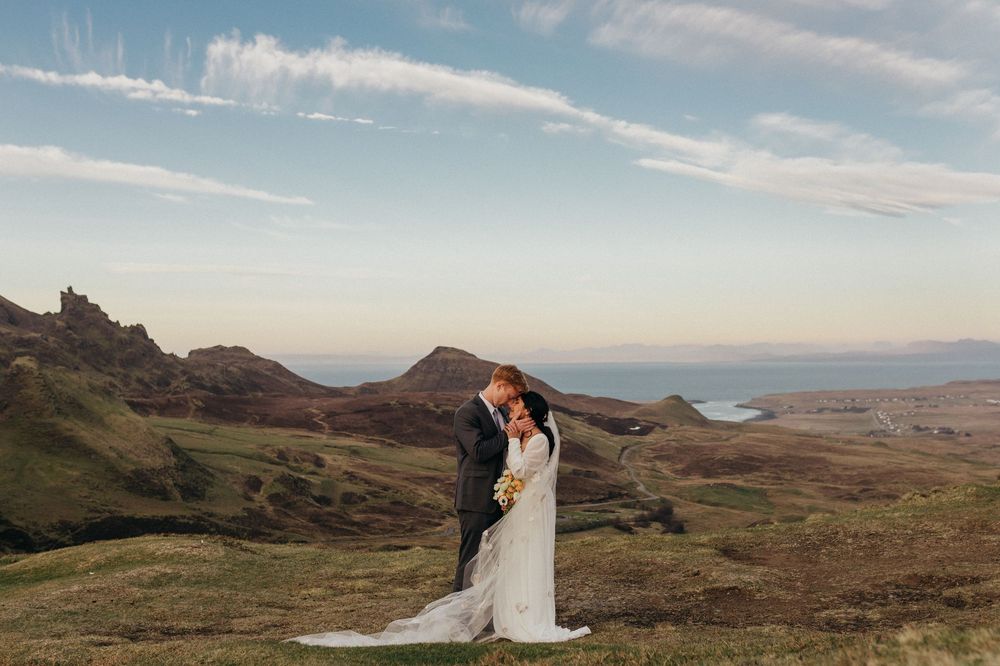 A couple shares an intimate moment on a hilltop overlooking scenic mountain landscapes at sunset.