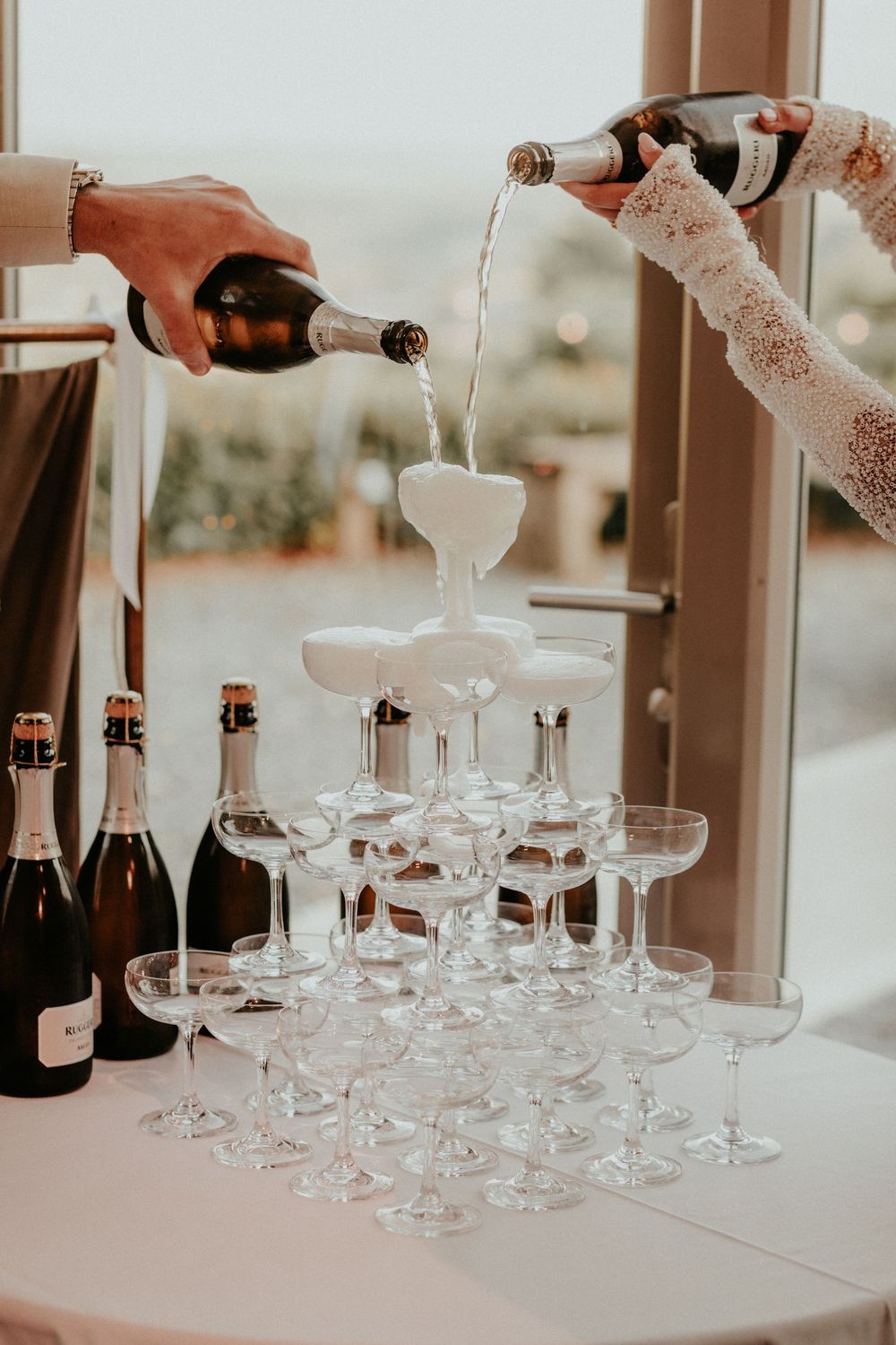 Champagne being poured into a tower of elegant coupe glasses at an upscale celebration event.
