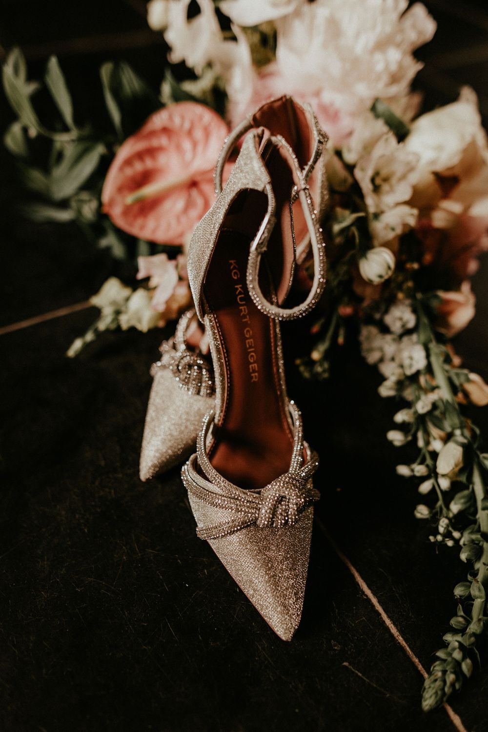 Sparkly pointed-toe wedding heels with bow details positioned near delicate floral arrangements.