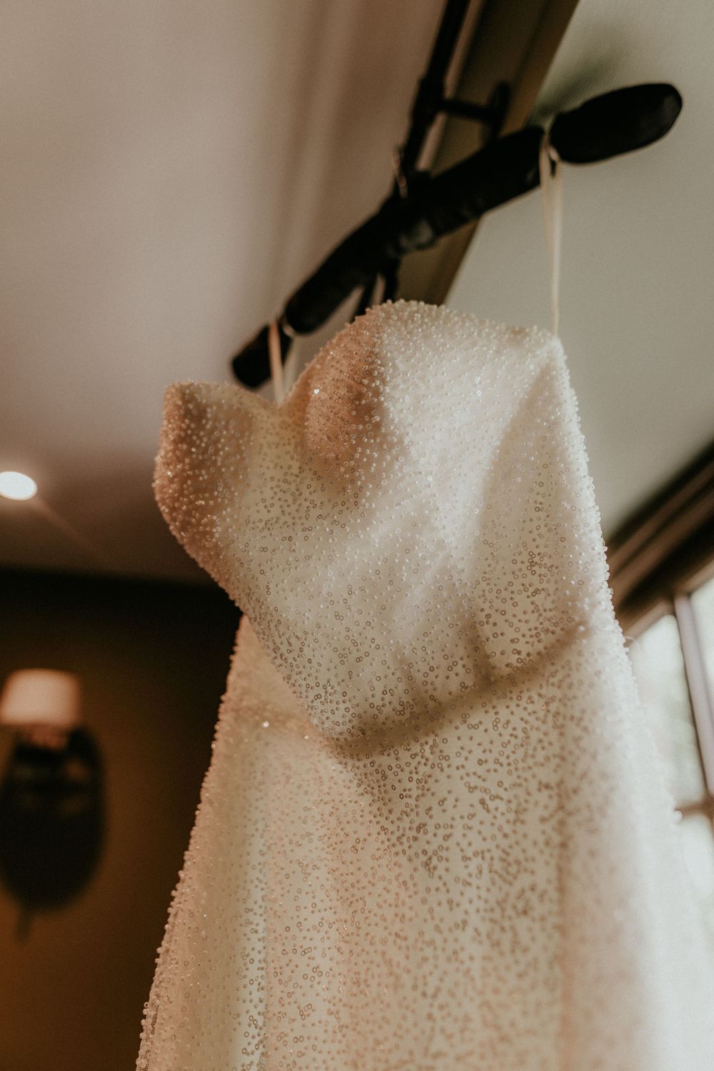A white textured wedding dress hanging on display in soft indoor lighting.