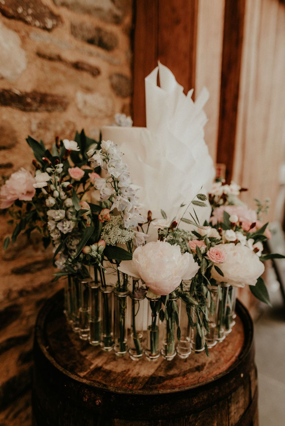 Wedding floral centerpiece with pink and white flowers arranged in glass vases on a rustic wooden barrel.
