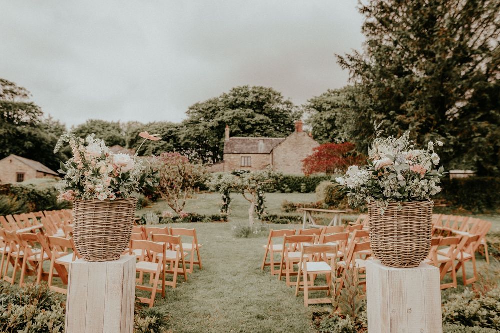 Outdoor garden wedding ceremony setup with white floral arrangements and wooden chairs on a lush green lawn.