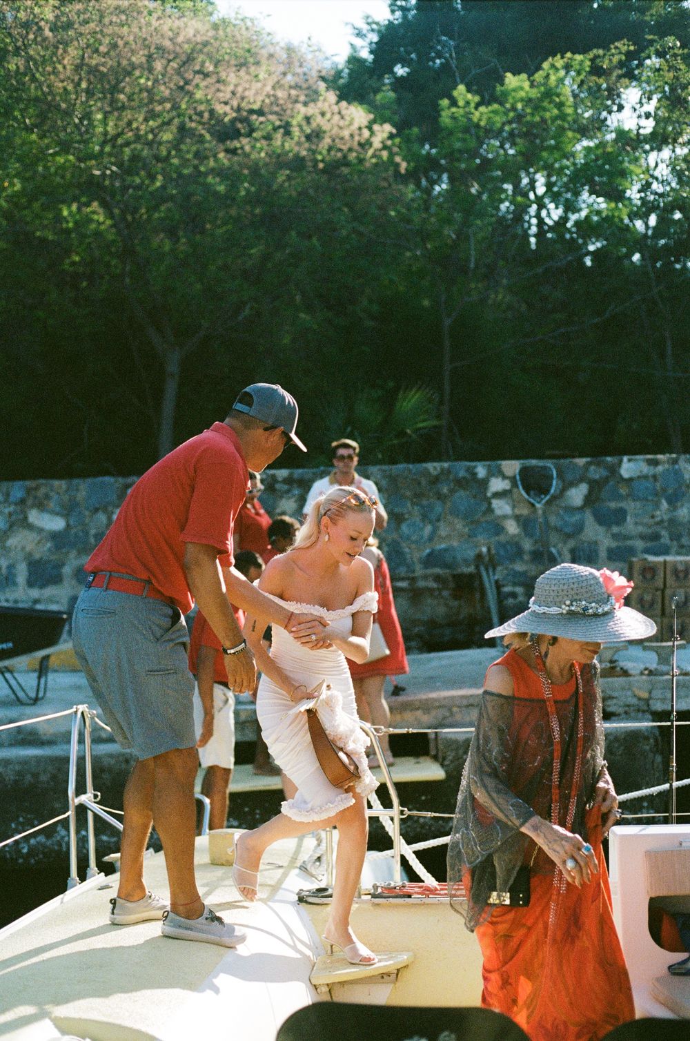 Passengers boarding a yacht on a sunny day with helpers assisting.