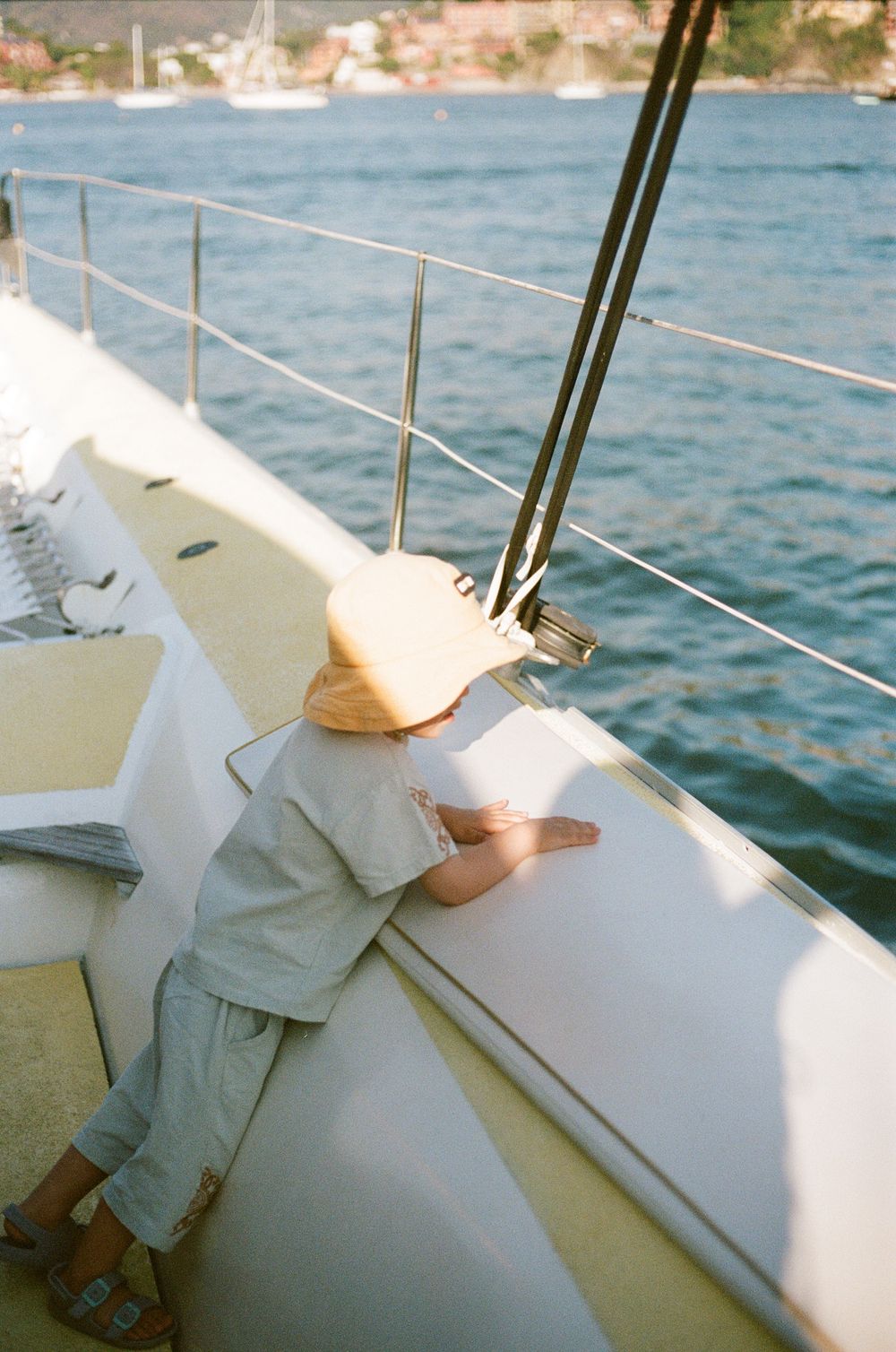 Small child in protective gear looking over the railing of a yacht at sea.