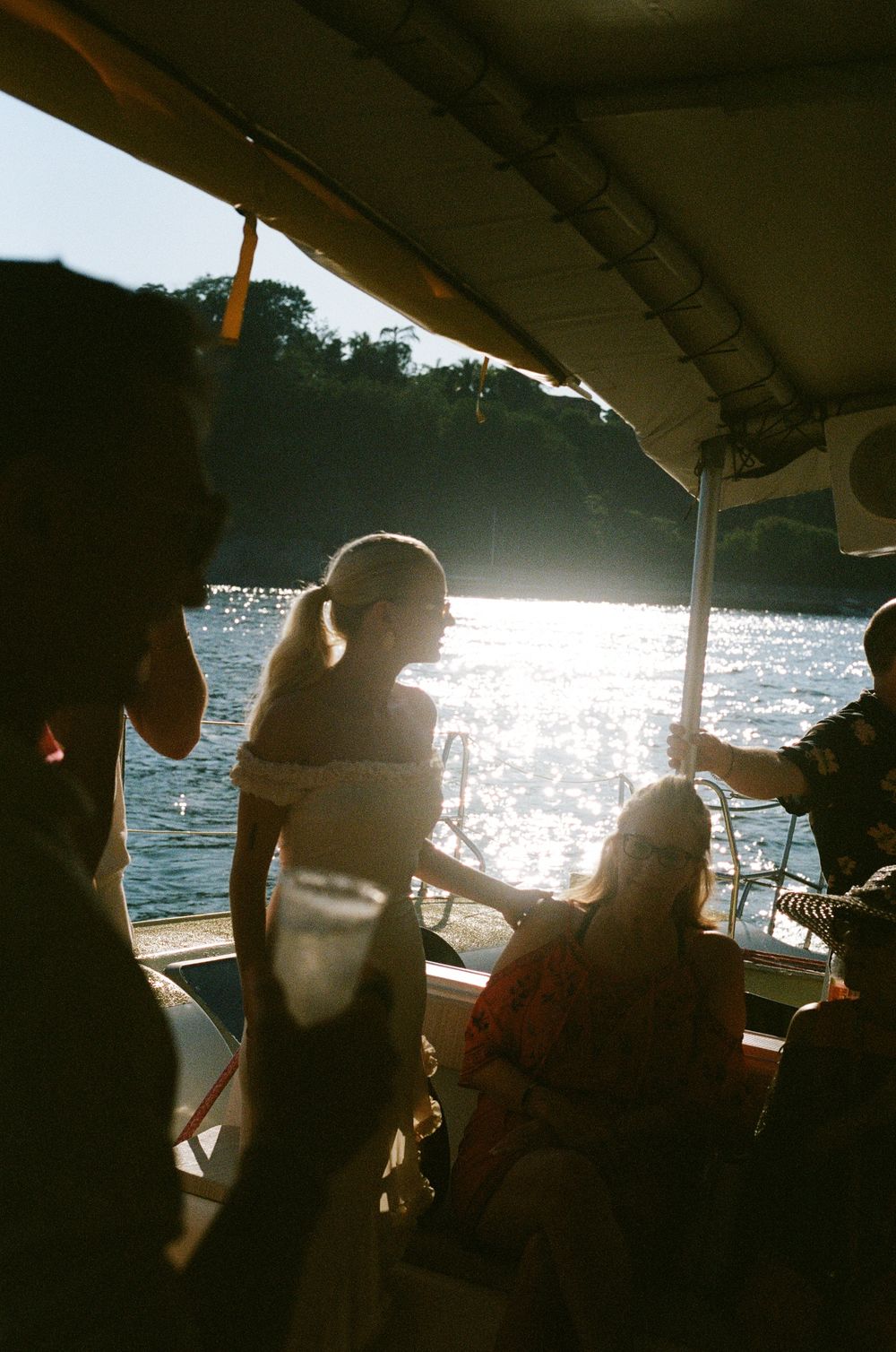 Passengers enjoying a boat ride on a sunny day with sparkling water and silhouettes against bright sunlight.