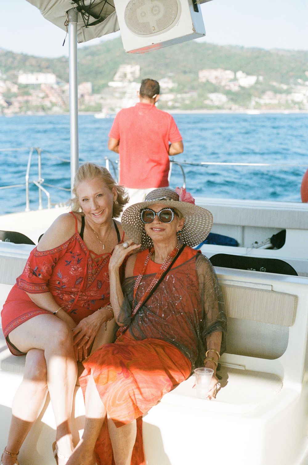 People relaxing on a boat deck with coastal scenery in the background on a sunny Mediterranean day.