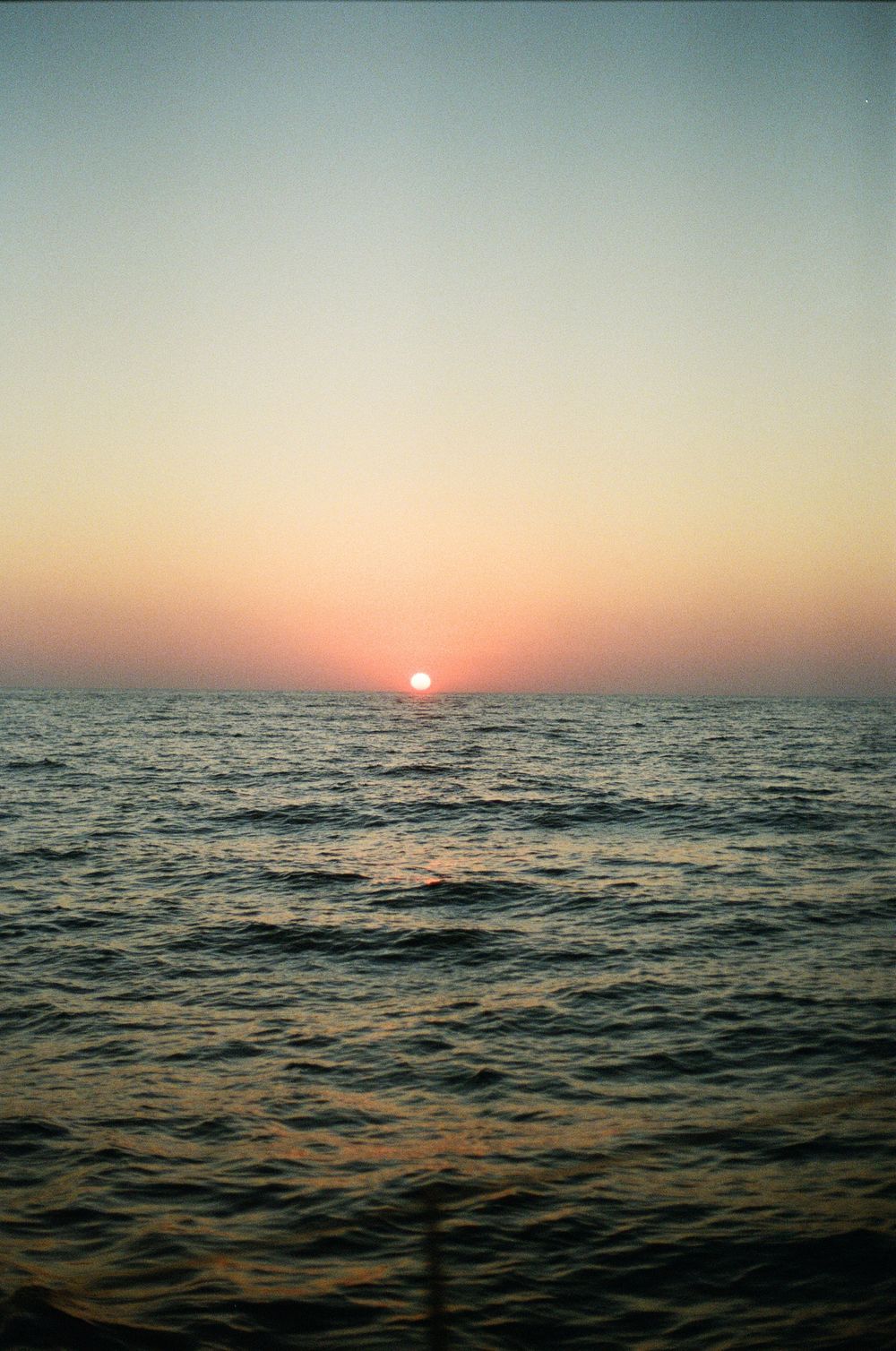 Sunset over calm ocean waters with sun touching the horizon creating golden reflections.