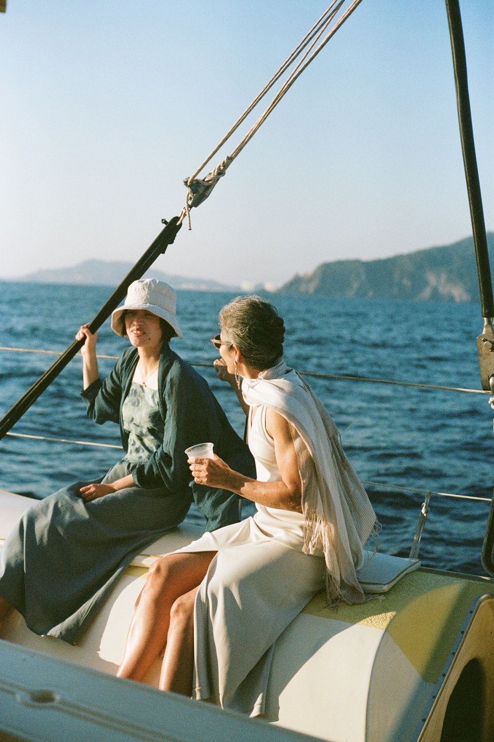 Two figures seated on a sailboat enjoying a conversation with mountains visible across the water.
