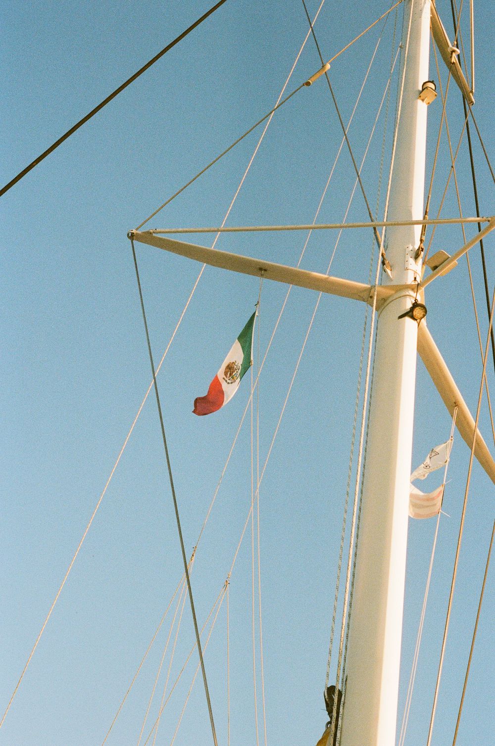Mexican flag flying from a sailboat mast against clear blue sky.