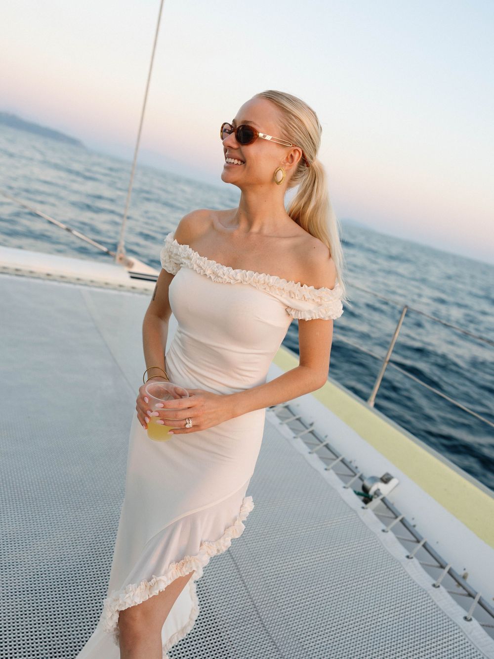 Woman in a white lace-trimmed dress poses on a boat deck against the ocean backdrop.