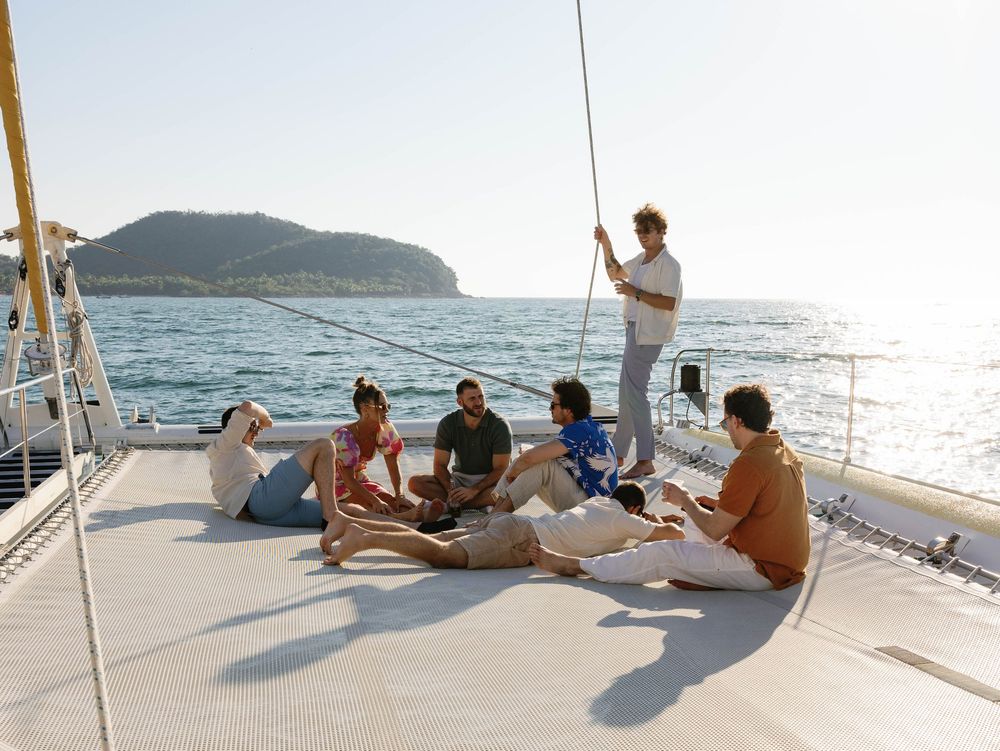 Group relaxing on a catamaran deck with coastal hills visible in the background.