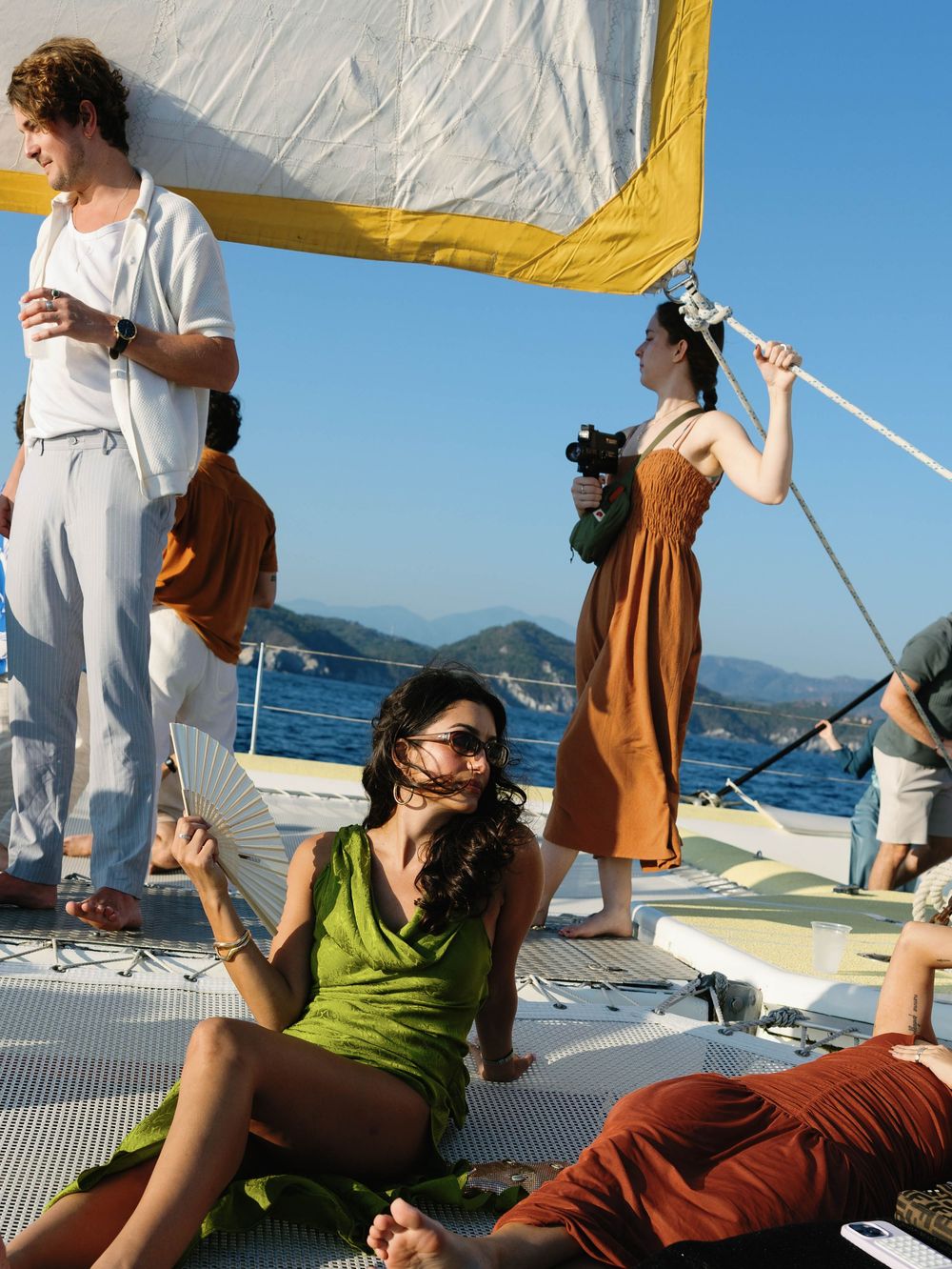 Casual gathering on sailboat deck with coastal mountains in background.