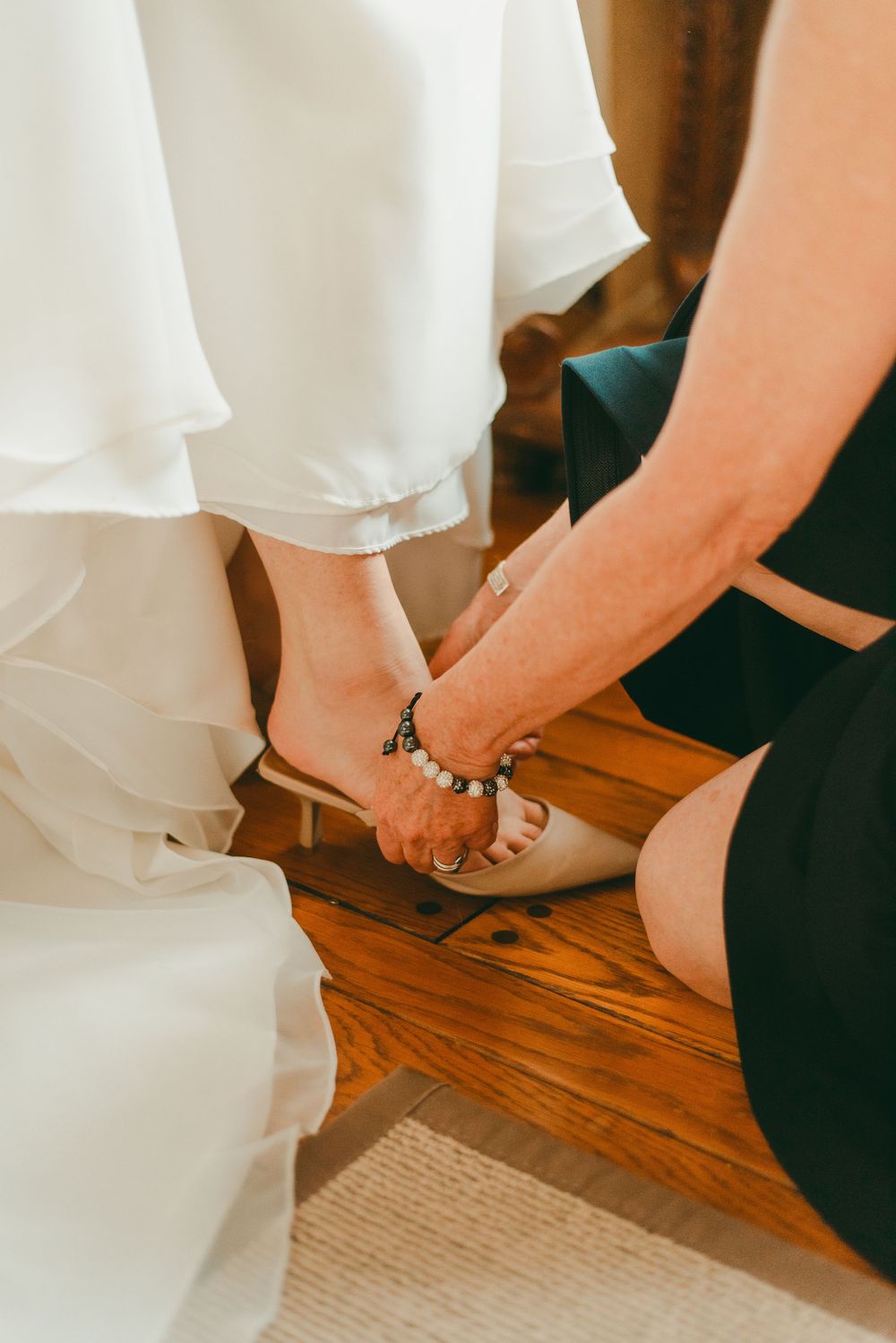 Mother of bride helps bride tie up shoe for wedding day