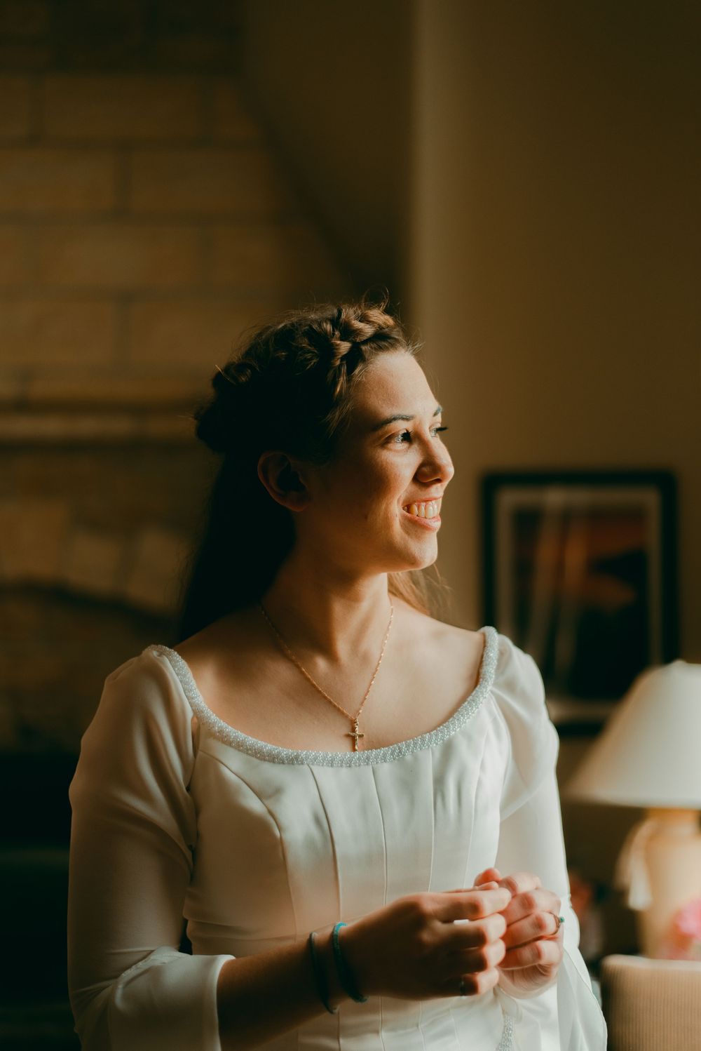 Bride getting ready and looking out window with soft natural light