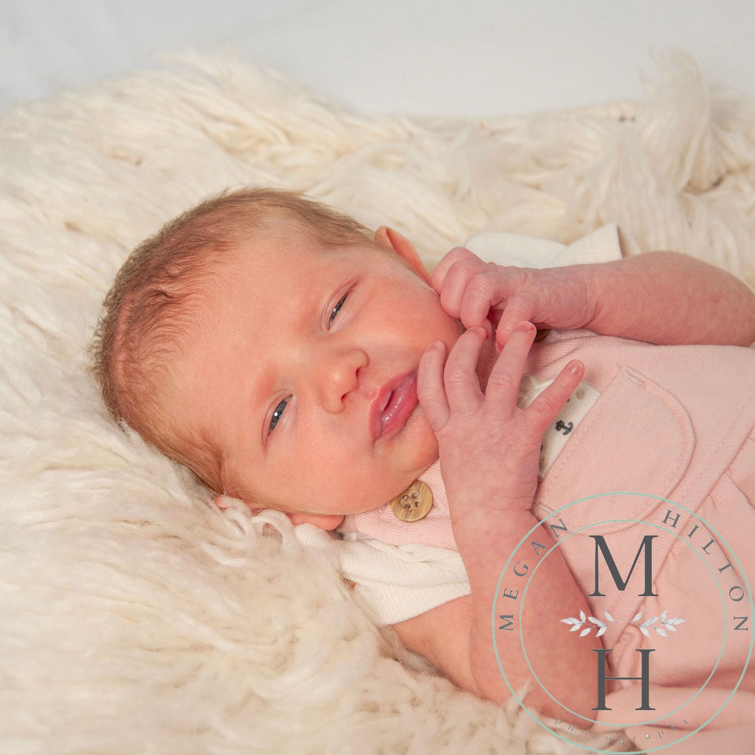 Photo of a newborn baby rests peacefully on soft white fur blanket in gentle natural lighting.