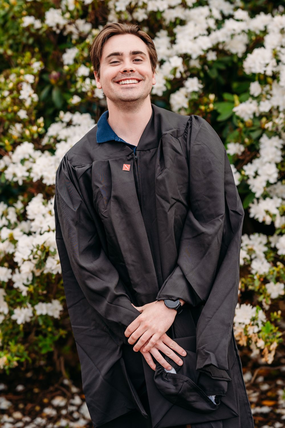 A person wearing a black jacket poses against a wall with white flowering bushes in four sequential photos.