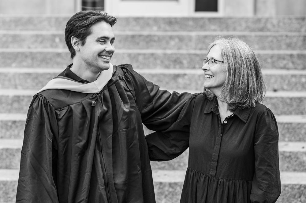 Group wearing graduation caps and gowns interact on stone steps during commencement.