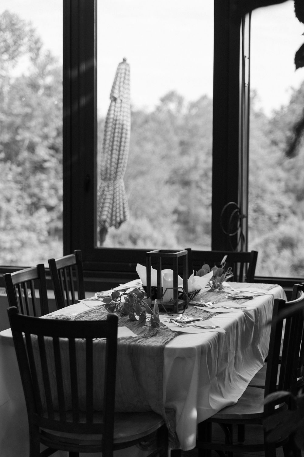 A black and white photo of an elegantly set dining table by a window with hanging decor.