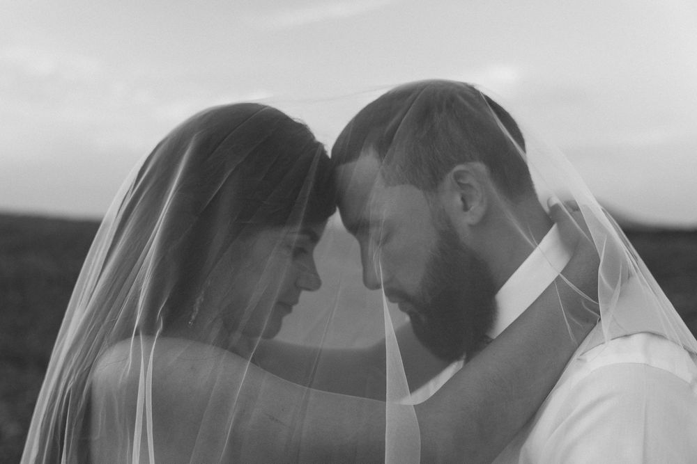 Intimate black and white portrait of couple sharing a tender moment under bridal veil.