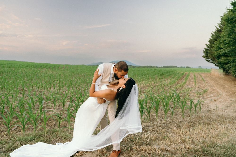 Wedding couple embraces in a dramatic dip pose with flowing veil in rural field setting.