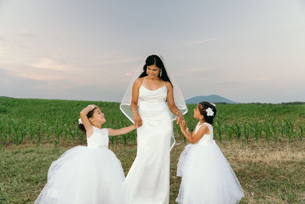 Three women in white dresses pose together in a sunlit field.