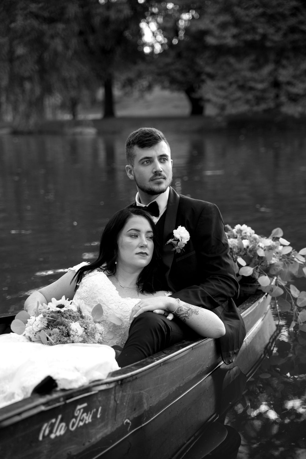 Romantic black and white portrait of couple in rowboat surrounded by flowers.