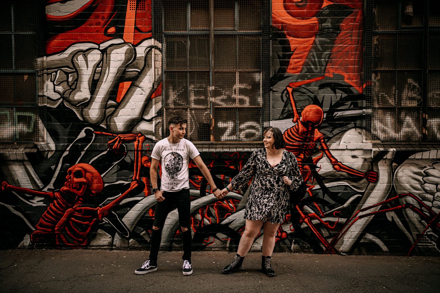 Couple dancing in front of urban graffiti wall featuring bold red and black street art in moody lighting.