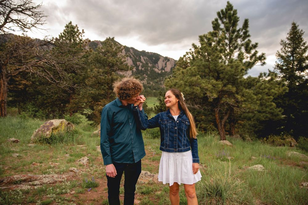 Two people enjoying a scenic moment together in a mountainous forest landscape with evergreen trees and rocky terrain.