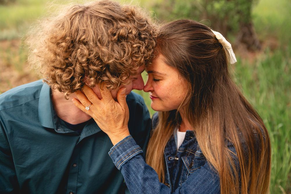 Two people share an intimate moment in nature as they huddle close together on a grassy backdrop.